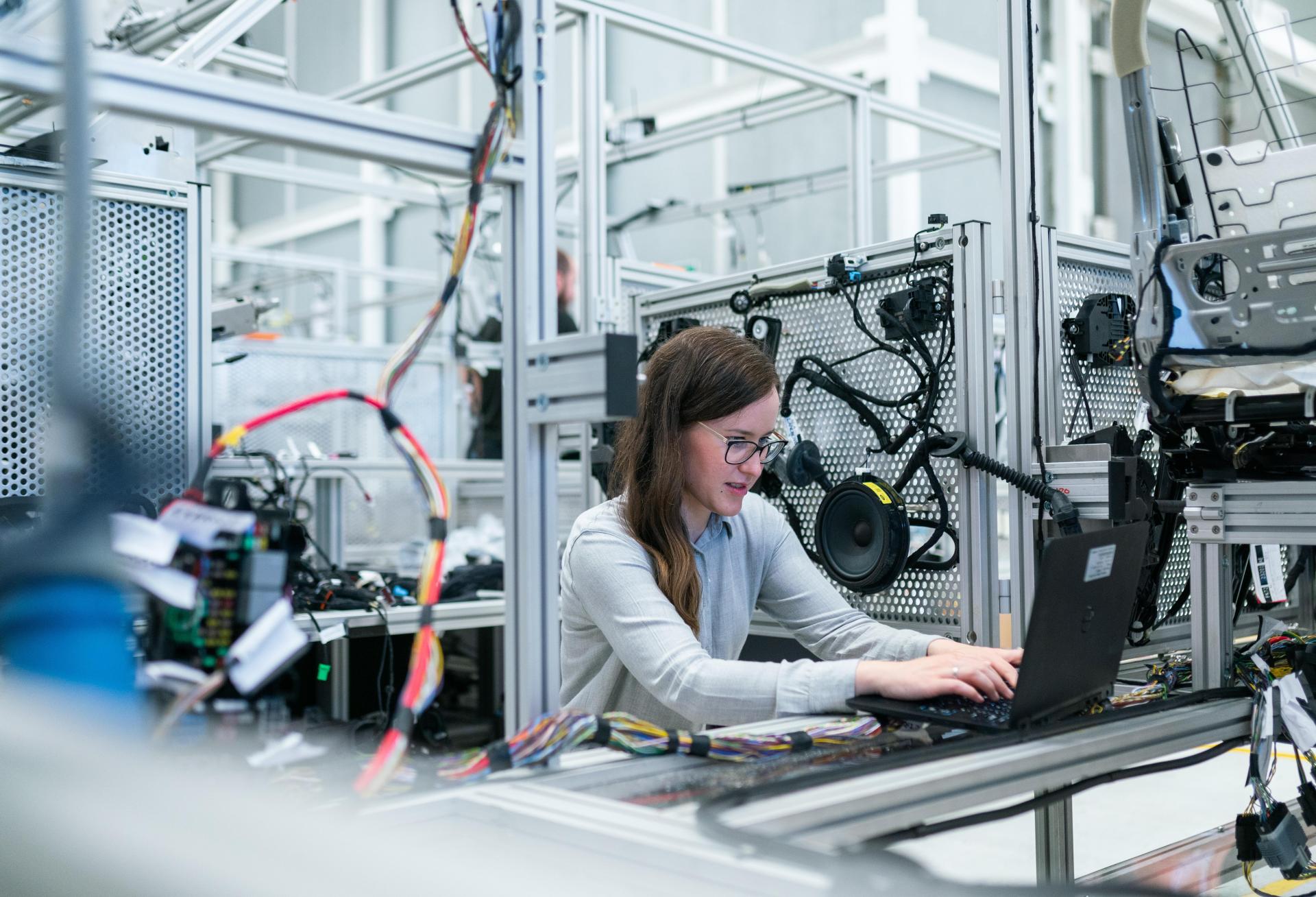 Engineer working on a laptop at an electronics test bench surrounded by wiring